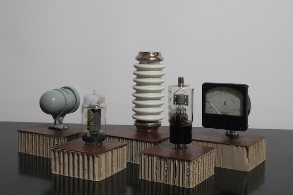 Auf dem Bild sind die Trophäen abgebildet. Senderöhren, Isolatoren, Verstärker jeweils auf einem Podest aus einer dünnen Holzplatte und Papplamellen.